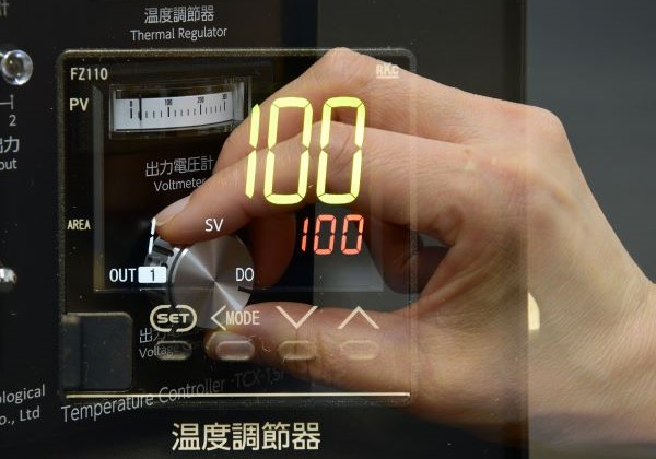 温度調節器の設定ボタンを指で操作している様子。表示は100